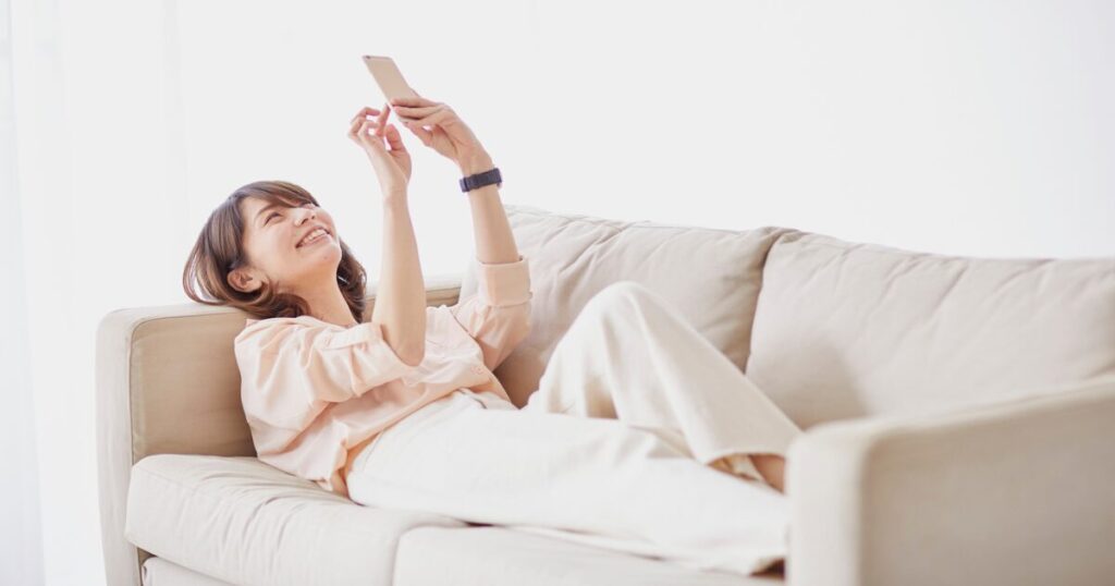 ソファでリラックスしてスマホを操作する女性
