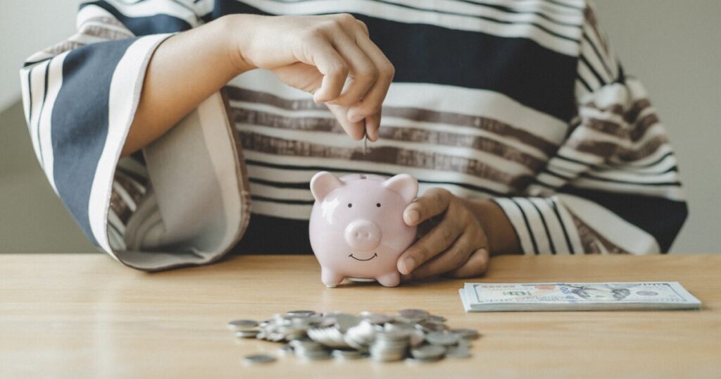ブタの貯金箱にお金を入れている女性